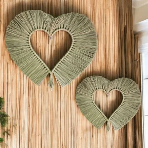 Two handcrafted heart-shaped wall hangings made from natural grass, displayed on a bamboo mat wall.