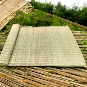 Handwoven natural rivergrass mat rolled out on bamboo surface in an outdoor rural setting