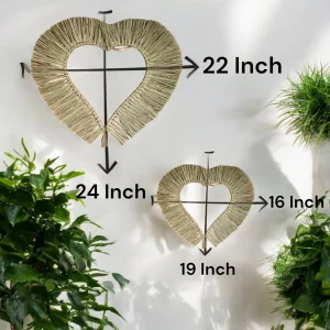 Heart-shaped natural grass wall hangings in two sizes, displayed against a white wall with green plants around.