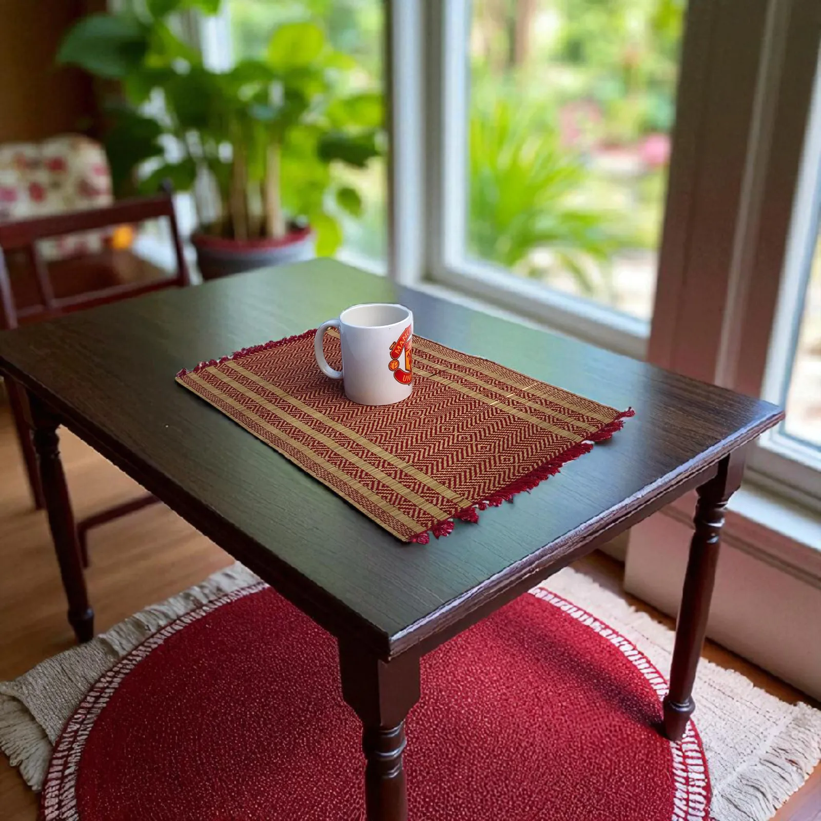 Handmade reed grass (madurkathi) table mat with red yarn design on wooden table – eco-friendly decor.