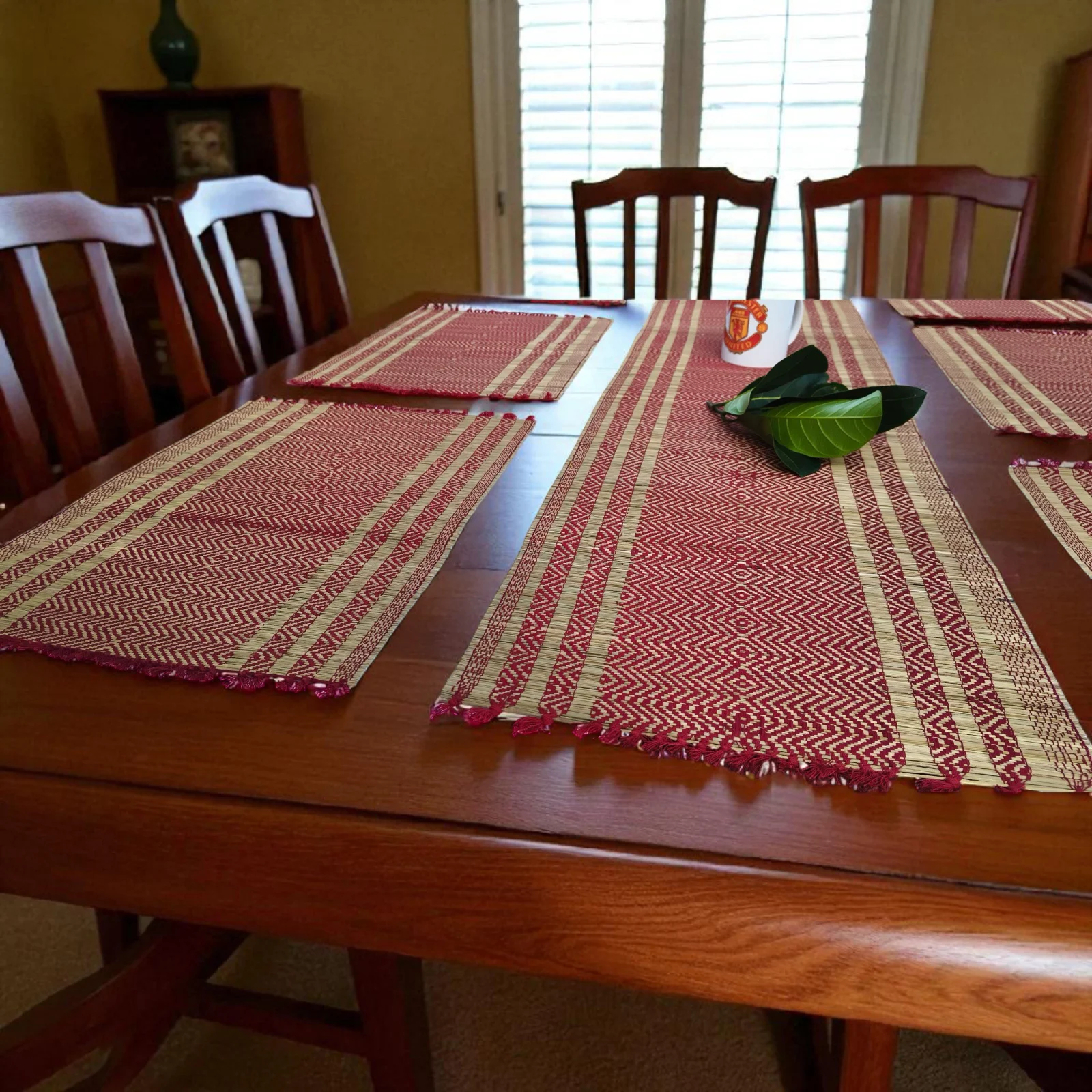 Handmade reed grass (madurkathi) table mat set with runner in red and natural straw color on wooden dining table.