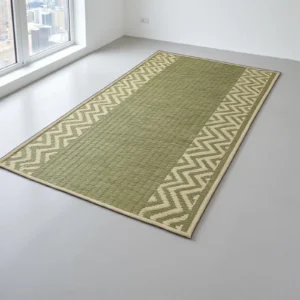 A long, rectangular Madurkathi grass mat in natural green with a zig-zag chevron border design, placed on a light gray floor near a large window.