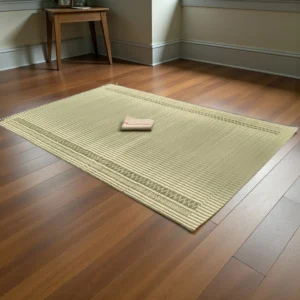 Handmade reed grass mat placed on a wooden floor in a cozy room, featuring natural beige-green weaving and a folded cloth on top.
