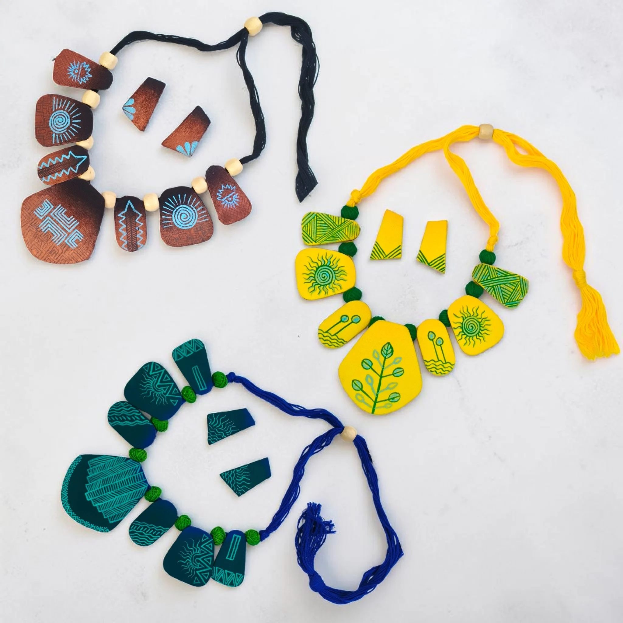 Handmade tribal fabric necklace sets in blue, yellow, and brown with matching earrings, boho statement jewelry collection on white background