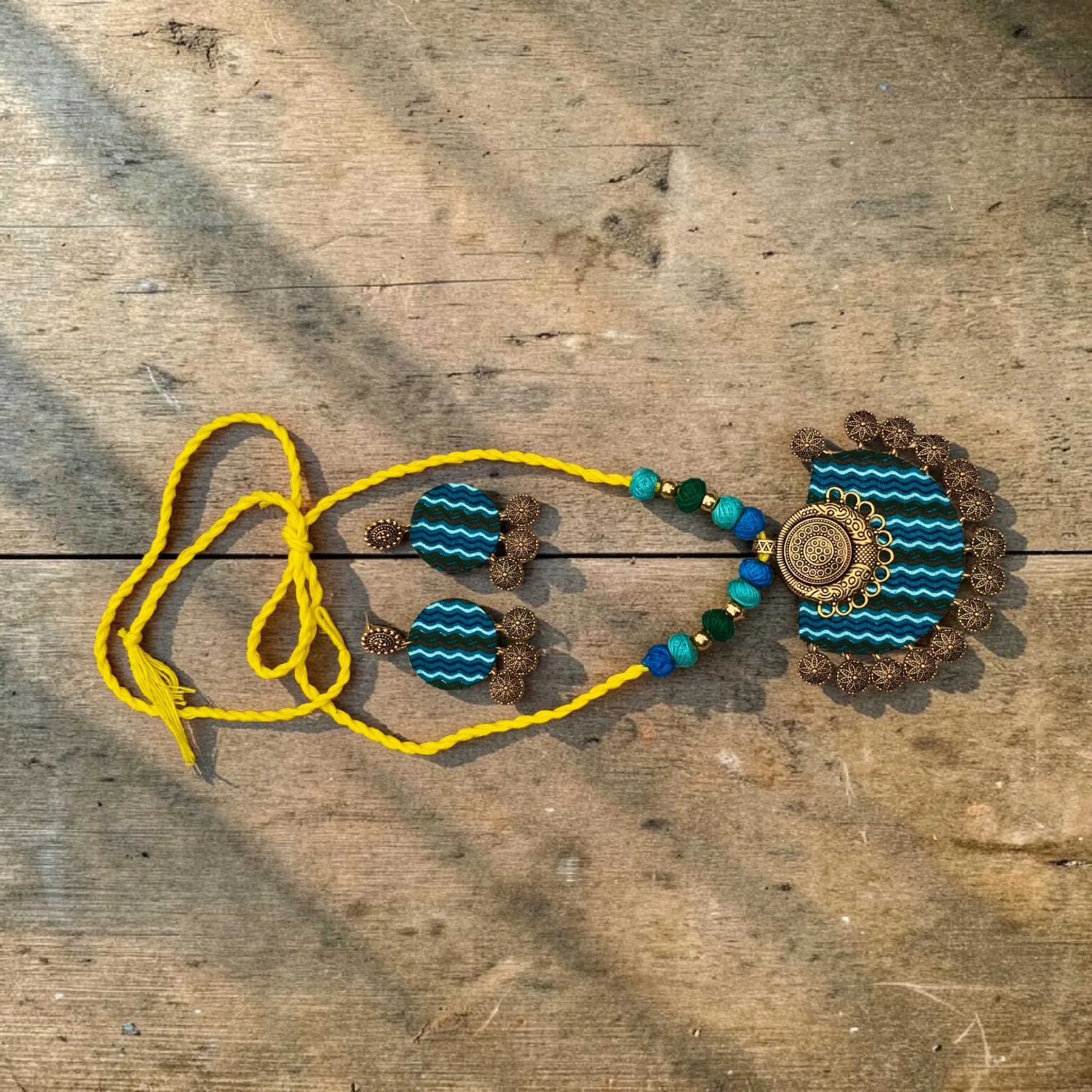 Handmade terracotta necklace set with teal striped pendant and matching earrings, yellow thread cord design on rustic wooden background