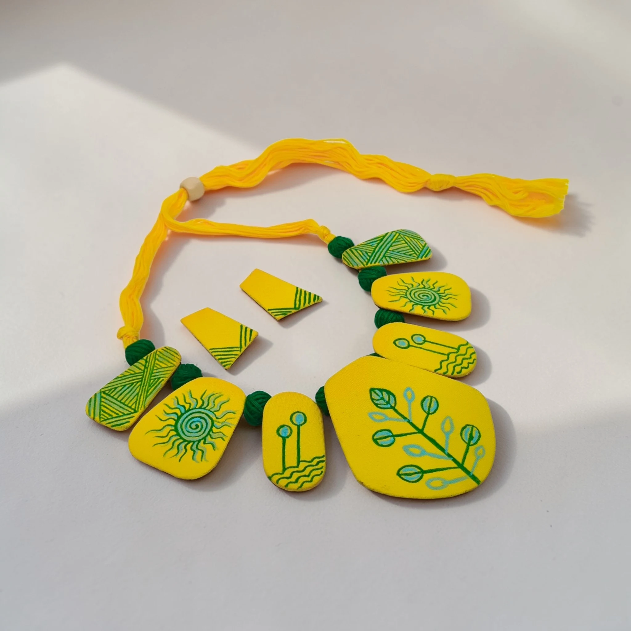 Handmade yellow tribal fabric necklace set with matching earrings on wood background, boho statement jewelry with hand-painted design