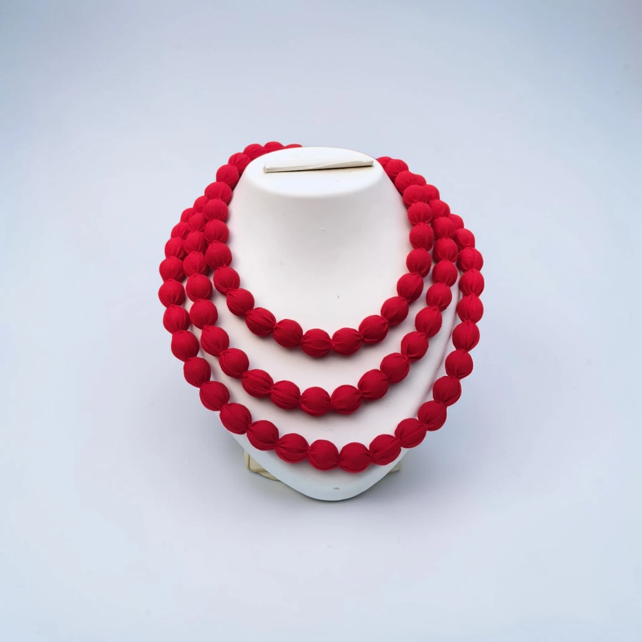 Handmade red fabric bead multi-layer necklace displayed on white stand minimal background