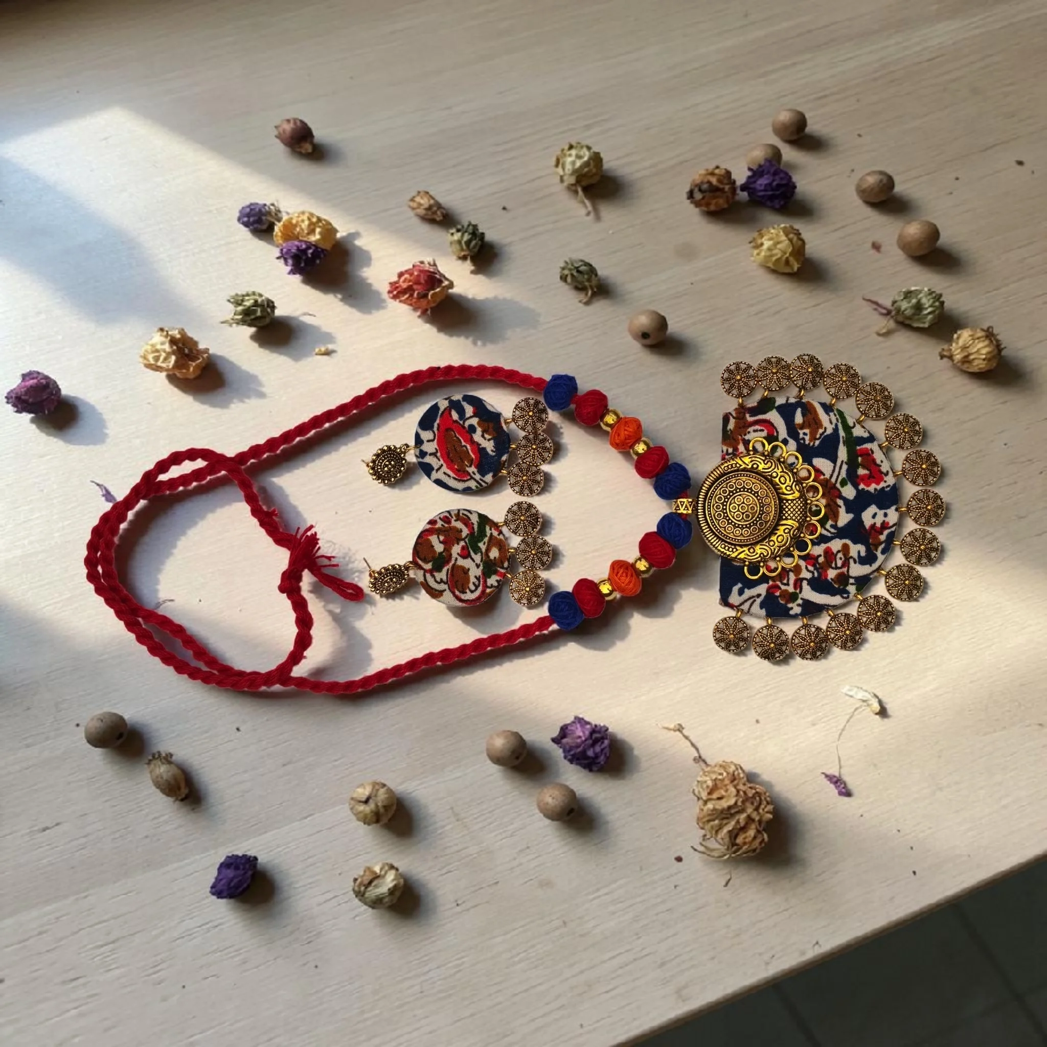 Handmade terracotta necklace set with floral fabric pendant and matching earrings, red thread cord design displayed on white textured background