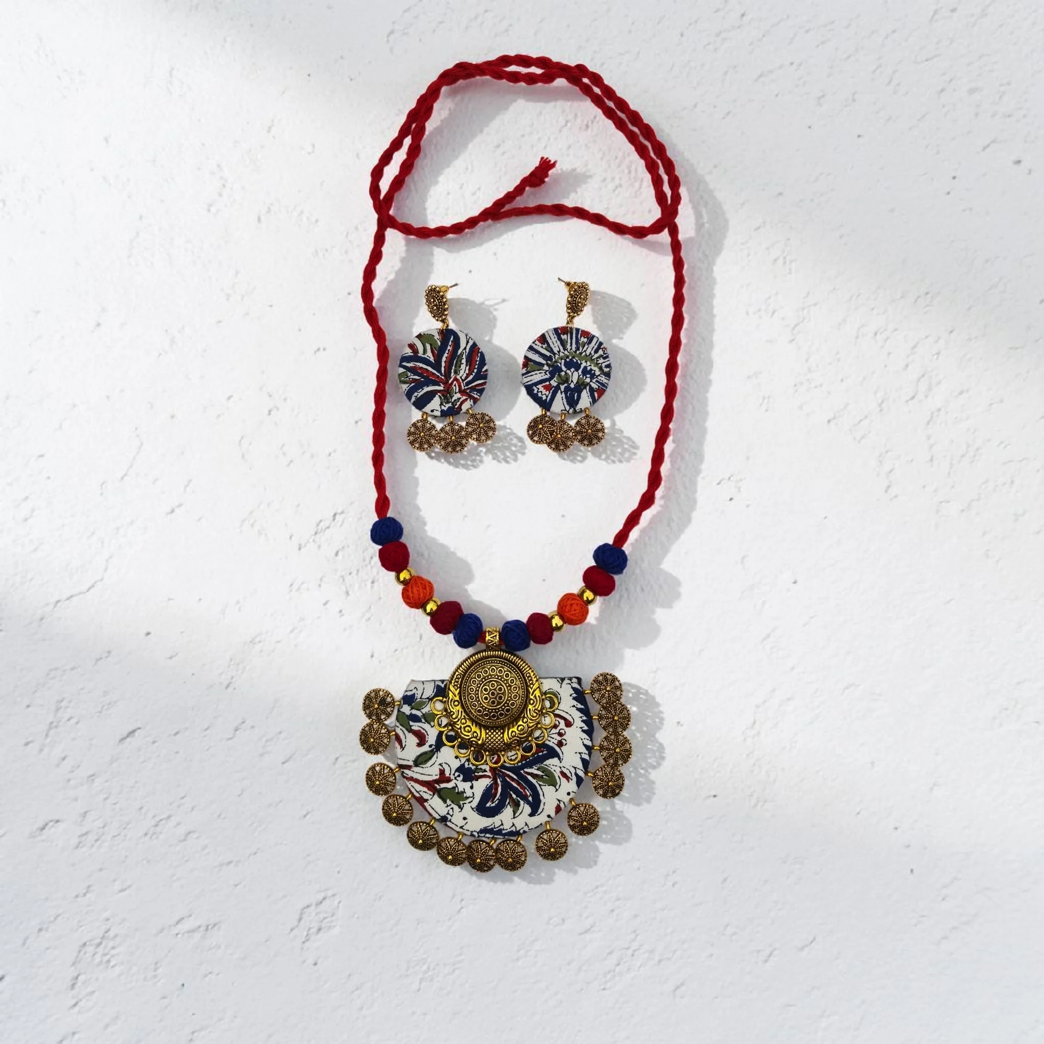 Handmade terracotta necklace set with floral fabric pendant and matching earrings, styled with red thread beads on wooden surface with dried flowers
