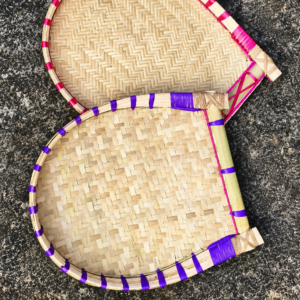 Set of two handmade bamboo Kulo baskets with traditional woven patterns, natural bamboo finish, and colorful pink and purple bindings, displayed on a rustic dark surface.